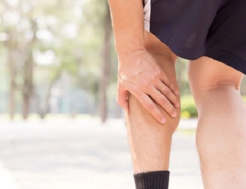 Một người đang xoa bóp chân, có thể là do căng cơ hoặc mỏi mệt sau một trận đấu, minh họa các nguyên nhân và cách chữa trị cần thiết sau khi đá bóng xong cần làm gì