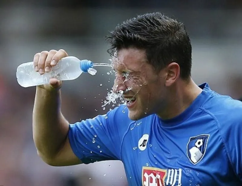 Một cầu thủ bóng đá đang uống nước khoáng để bù điện giải sau khi tập luyện cường độ cao, giúp duy trì thể lực và hiệu suất